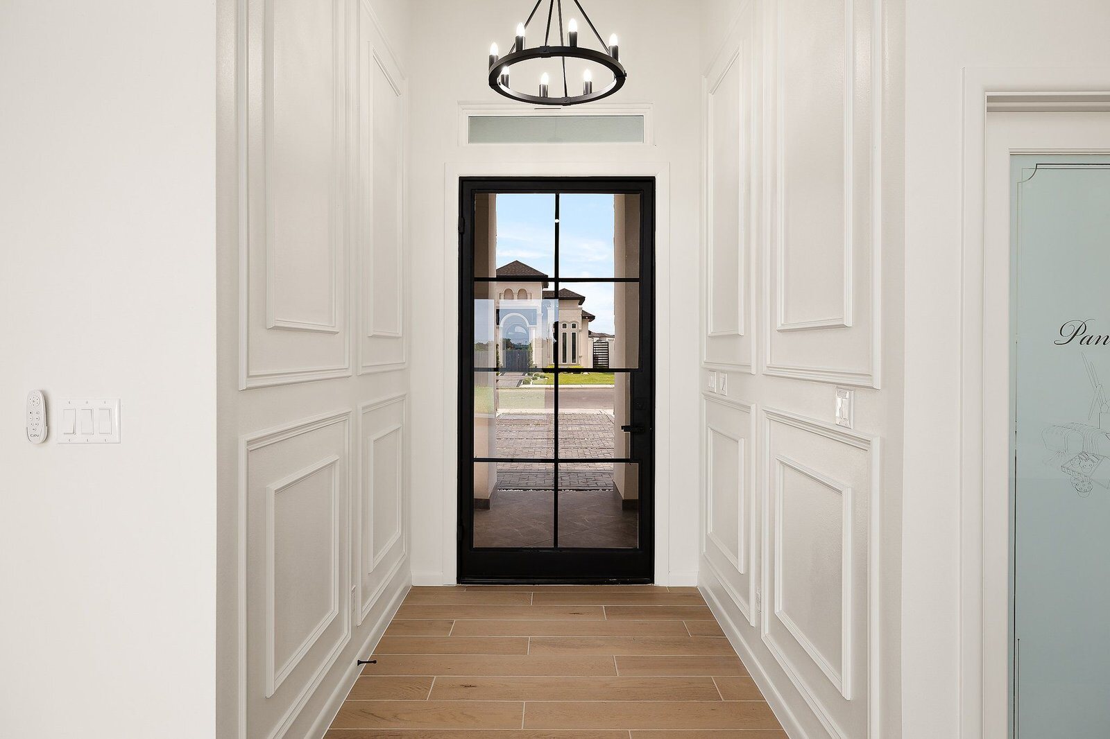 Entry hall with paneled white walls, a black steel front door and light oak floors.